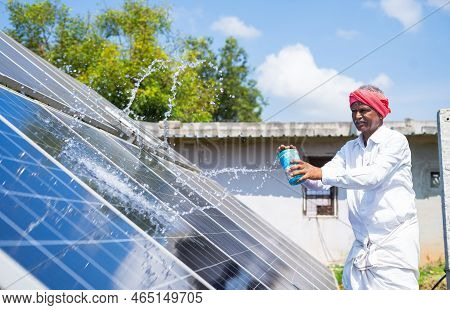 Indain Village Farmer Cleaning With Water On Solar Panels At Farmland - Concept Of Renewable Energy,