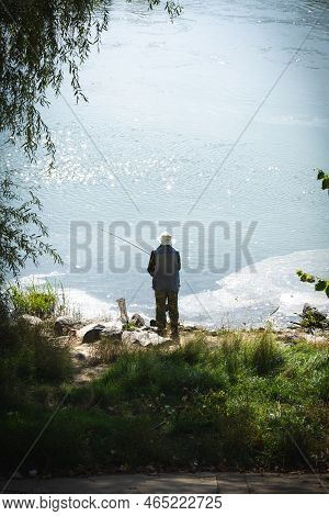 Undefined Man Is Fishing In The Dniester River. Dirty Film Of Sewage Near The Banks Of The Dniester 