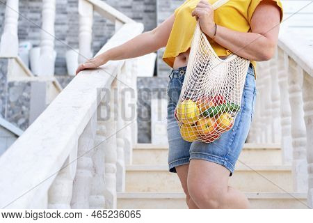 Anonymous Woman Holding Mesh Bag Full Of Fruit And Vegetables.