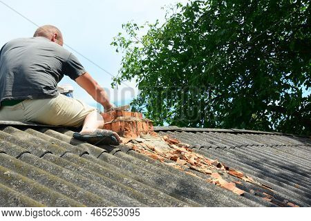 Old House Brick Chimney Rebuilding. A Roofing Contractor On Asbestos Roof Is Removing Bricks Of A Da