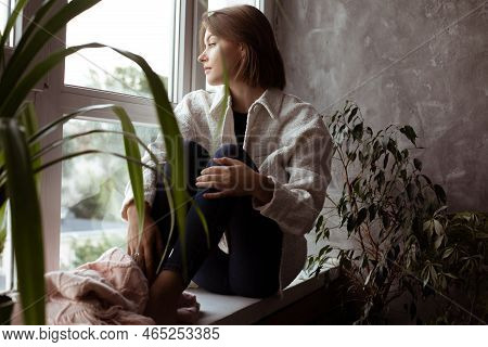 Calm, Thoughtful Romantic Young Woman Looking Out Window, Sit On Windowsill In Warm Clothes. Dreams 