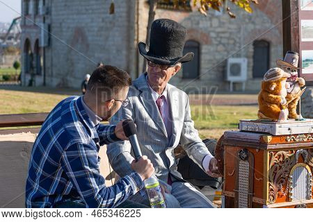 Bendery, Moldova - November 12, 2022: Organ Grinder In A Hat And Round Glasses Gives An Interview On