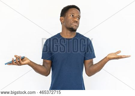 Doubtful Man Spreading Arms. Young African American Male Model In Blue T-shirt Holding Smartphone An