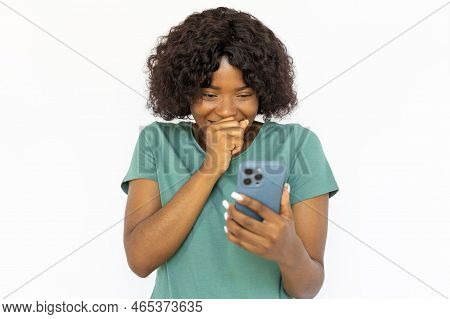 Pretty Young Woman With Smartphone Chuckling Merrily. Joyful African American Girl Watching At Smart