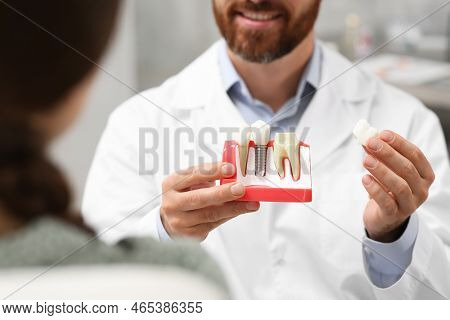 Doctor With Educational Model Of Dental Implant Consulting Patient In Clinic, Closeup