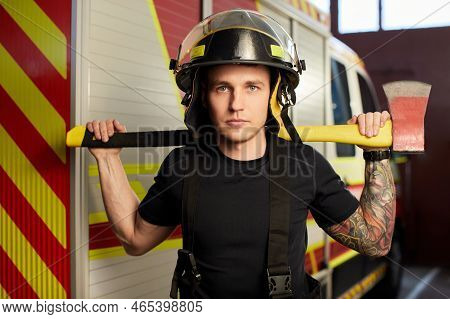 Photo Of Fireman Wearing Helmet With Ax Against Fire Engine.