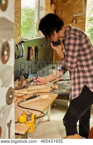Cheerful Carpenter Woman Discussing Order Details With Her Customer On Smartphone