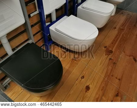 Exhibition Of Samples Of White Toilet Bowls Standing In A Row In The Warehouse Of A Plumbing Store. 