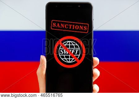 Ukraine, Kiev - February, 23 2022: Hand Holding Mobile With Crossed Out Swift Logo And Russian Flag 
