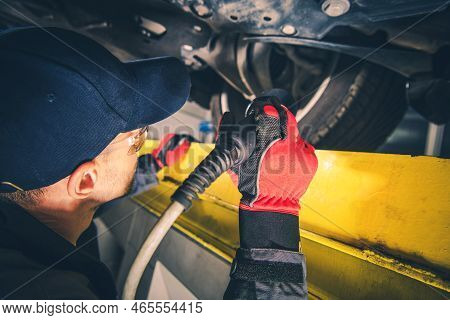 Professional Mechanic Checking Vehicle Undercarriage Using A Flashlight During Scheduled Car Inspect