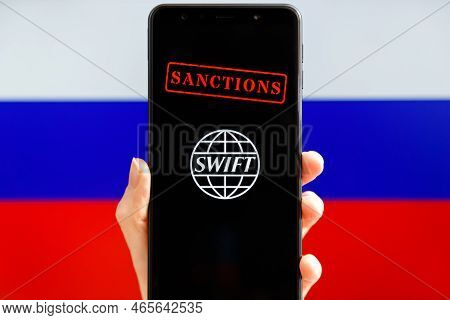 Ukraine, Kiev - February, 23 2022: Hand Holding Mobile With Swift Logo, Sanctions And Russian Flag I