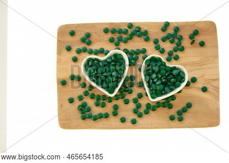 Spirulina Algae Tablets In Cups In The Shape Of A Heart On A Wooden Board On A White Background.vita