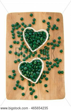 Spirulina Algae Tablets In Cups In The Shape Of A Heart On A Board On A White Background.vitamins An