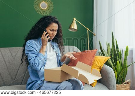 Nervous Young Beautiful Latin American Woman Is Begging On The Phone At Home On The Sofa, Holding A 