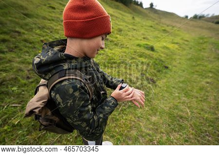 Boy With Bacpack Looking At His Smart Watches While Hiking.