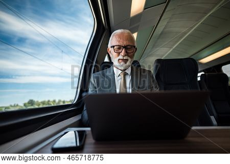 Smiling Senior Businessman Working On Laptop While Sitting By Window On The Passenger Train. Elderly
