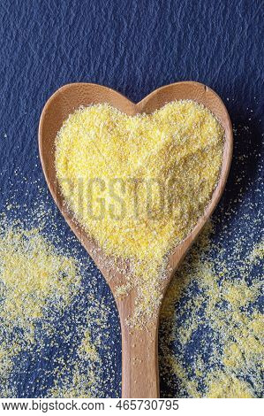 Yellow Cornmeal In Heart-shaped Spoon On Black Table. Flat Lay, Copy Space