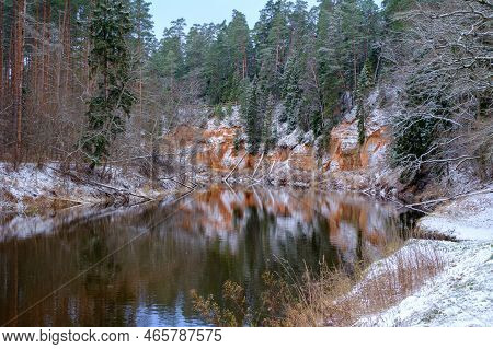 View Of Red Sandstone Cliffs. Salaca River. Skanaiskalns Nature Park. November Is The First Snow In 