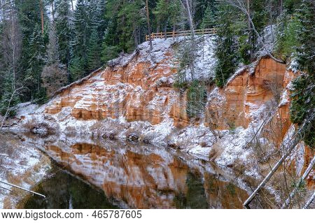 View Of Red Sandstone Cliffs. Salaca River. Skanaiskalns Nature Park. November Is The First Snow In 