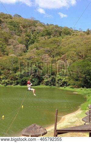 Photo Of A Woman Ziplining With Trees, Lake, Wooden Deck And A Blue Sky. Ideal Summer Day To Enjoy T