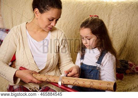 Young Mother And Little Girl Daughter Using Paper For Wrapping Packing Christmas New Year Presents, 