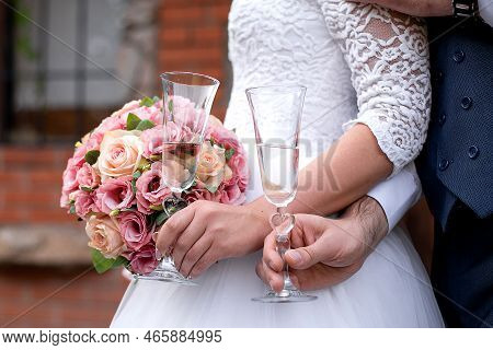 Wedding Bouquet In The Hands Of The Bride And Groom At The Ceremony. Glasses Of Champagne. Floristry