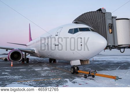 Jet Plane With Towbar Near The Boarding Bridge At Winter Airport Apron