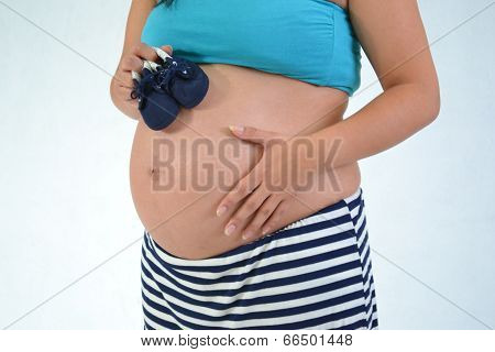 Pregnant woman with baby´s shoes touching her gut