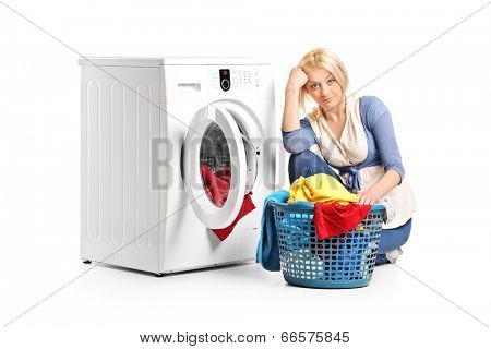Bored woman sitting by a washing machine and doing laundry isolated on white background