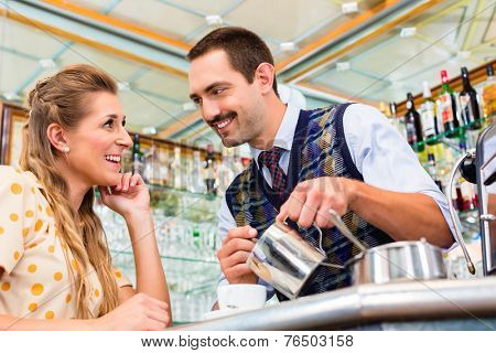 Girl in cafe or coffee bar flirting with barista who is busy preparing Cappuccino with professional machine