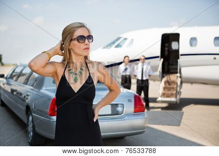 Wealthy woman in elegant dress standing against limousine and private at terminal