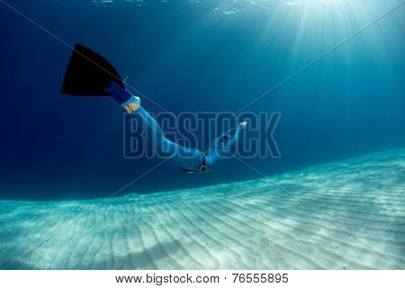 Lady free diver swimming in monofin over sandy bottom