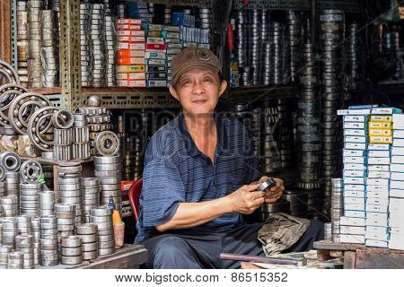 CAN THO, VIETNAM, DECEMBER 11, 2014: Portrait of A ball bearing seller cleaning a stuff in the Tan An market streets in Can Tho city, Vietnam.