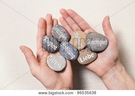 Inner balance concept: hands holding stones with german words for: hope, courage, intelligenz, justice, equality, love and temperance, 