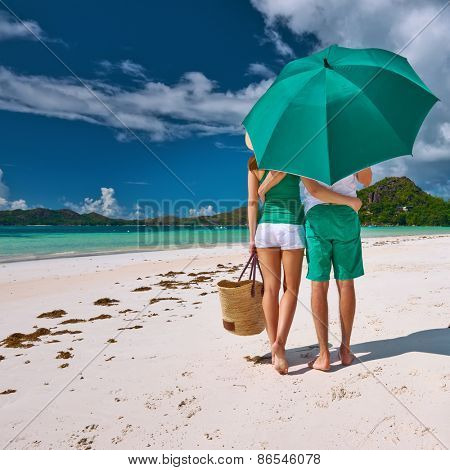 Couple in green with umbrella on a tropical beach at Seychelles