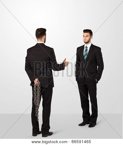 Two opposing businessman shake hands, one of them hiding a weapon behind his back