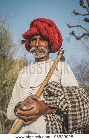 GODWAR REGION, INDIA - 13 FEBRUARY 2015: Rabari tribesman holds traditional ax on field and watches herd. Post-processed with grain, texture and colour effect.