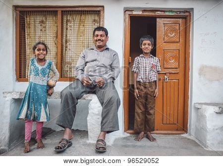 KAMALAPURAM, INDIA - 02 FABRUARY 2015: Father and his two children in front of their home in a town close to Hampi. Post-processed with grain, texture and colour effect.