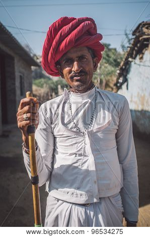 GODWAR REGION, INDIA - 13 FEBRUARY 2015: Rabari tribesman stands in courtyard of home wearing traditional clothes and holds herding stick. Post-processed with grain, texture and colour effect.