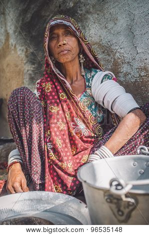 GODWAR REGION, INDIA - 13 FEBRUARY 2015: Rabari tribeswoman in sari decorated with traditional upper-arm bracelets cleans dishes. Post-processed with grain, texture and colour effect.
