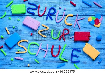 the sentence zuruck zur schule, back to school in german, written with modelling clay of different colors on a blue rustic wooden background