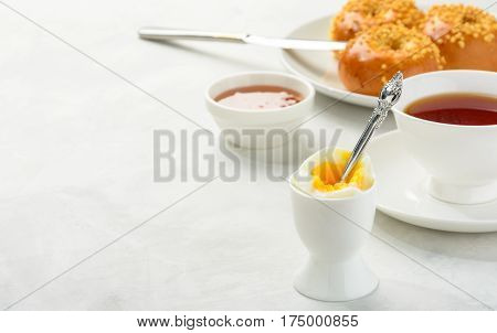 Delicious and healthy breakfast of boiled egg and brioche buns with black tea on a light background. Copy spacesoft focus.