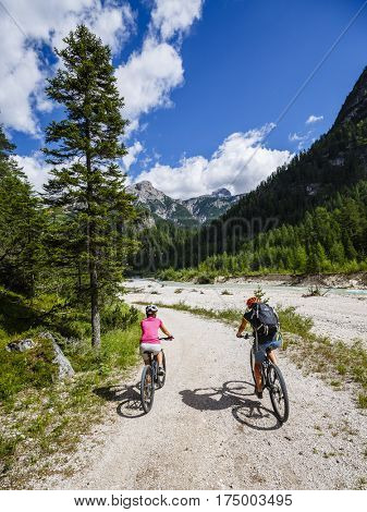 Mountain biking woman and young girl along river in Dolomites, Italy