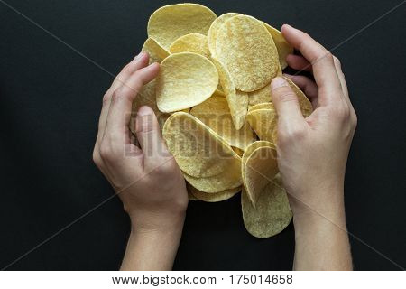 Pile of potato chips and women hands on a black background. Photography of fast food