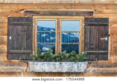 Vintage Window of old alpine house. Wooden rustic background. Reflections of snow spotted mountains in window glass.