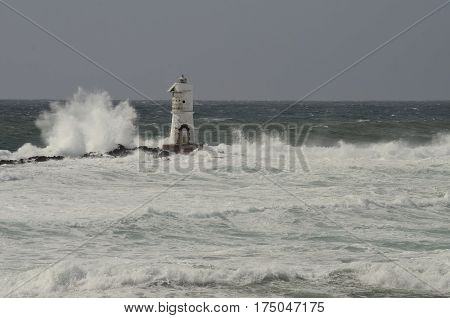 Lighthouse in the wind, wave in the left, grey sky, white water.