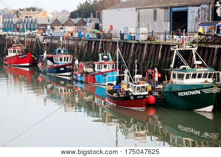 WHITSTABLE, UK -February 24, 2017: Fishing Boats in Whitstable Harbour in portrait view with warehouse in background