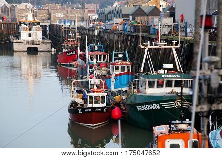 WHITSTABLE, UK -February 24, 2017: Fishing Boats in Whitstable Harbour in portrait view with warehouse in background