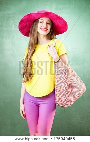 Colorful portrait of a beautiful woman in yellow t-shirt and pink hat with shopping bag on the green background