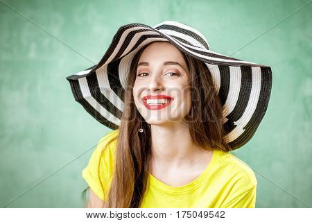 Colorful portrait of a beautiful woman in yellow t-shirt and striped hat on the green background
